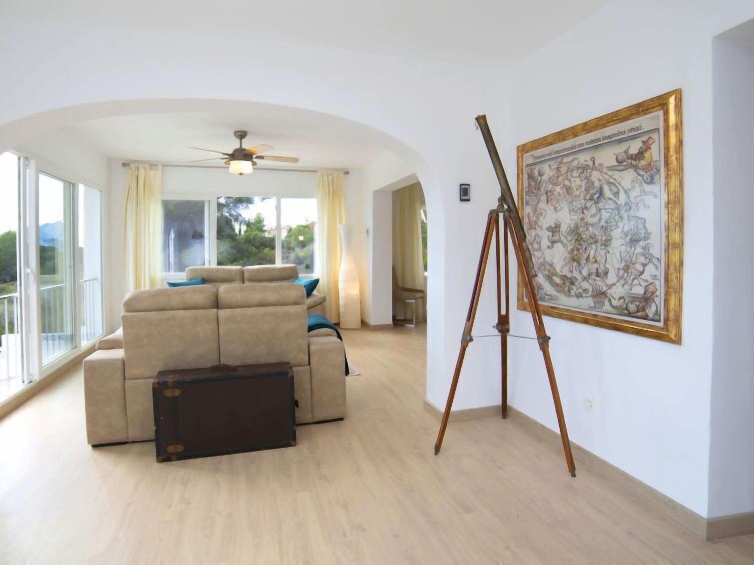 A spacious living room with a large sofa, a standing fan, and a tripod with a painting.