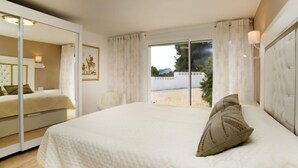 Ein Schlafzimmer mit einem großen Bett, einem Spiegel, einem Fenster mit Vorhängen und Blick ins Freie.