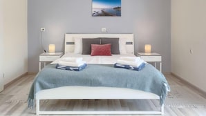 Une chambre moderne avec un lit blanc, des murs gris et un tableau encadré au-dessus du lit.