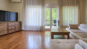 Un salon spacieux doté d’un plancher en bois, d’un téléviseur à écran plat posé sur un meuble en bois, d’un canapé beige et d’une table basse.