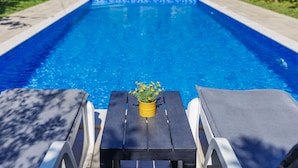 Une piscine avec des chaises longues et une table agrémentée d’une plante en pot.