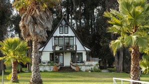 A two-story house with a balcony, surrounded by palm trees and a grassy lawn. - Hotel Jardín del Lago (Las Cabras)