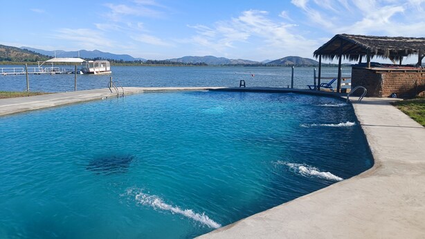 A swimming pool with a dock and a boat, surrounded by mountains and a clear sky. - Hotel Jardín del Lago (Las Cabras)