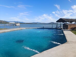 Una piscina con un muelle y un bote, rodeada de montañas y un cielo despejado.