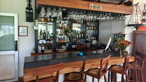 A bar area with wooden bar counter, multiple stools, and a variety of bottles and glasses. - Hotel Jardín del Lago (Las Cabras)
