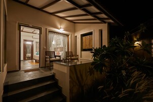 A modern house with a glass door leading to a living area, a staircase, and a small outdoor seating area with chairs.