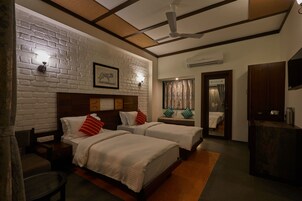 Habitación de hotel con dos camas, una pared de ladrillo, un ventilador de techo y un escritorio de madera.