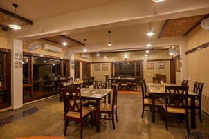 A restaurant with multiple dining tables and chairs, wooden beams on the ceiling, and air conditioning units.
