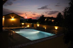 A rectangular swimming pool with a tiled deck, surrounded by walls with exterior lighting.