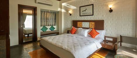 A hotel room with a large bed, a wooden headboard, a glass table, and a brick wall.