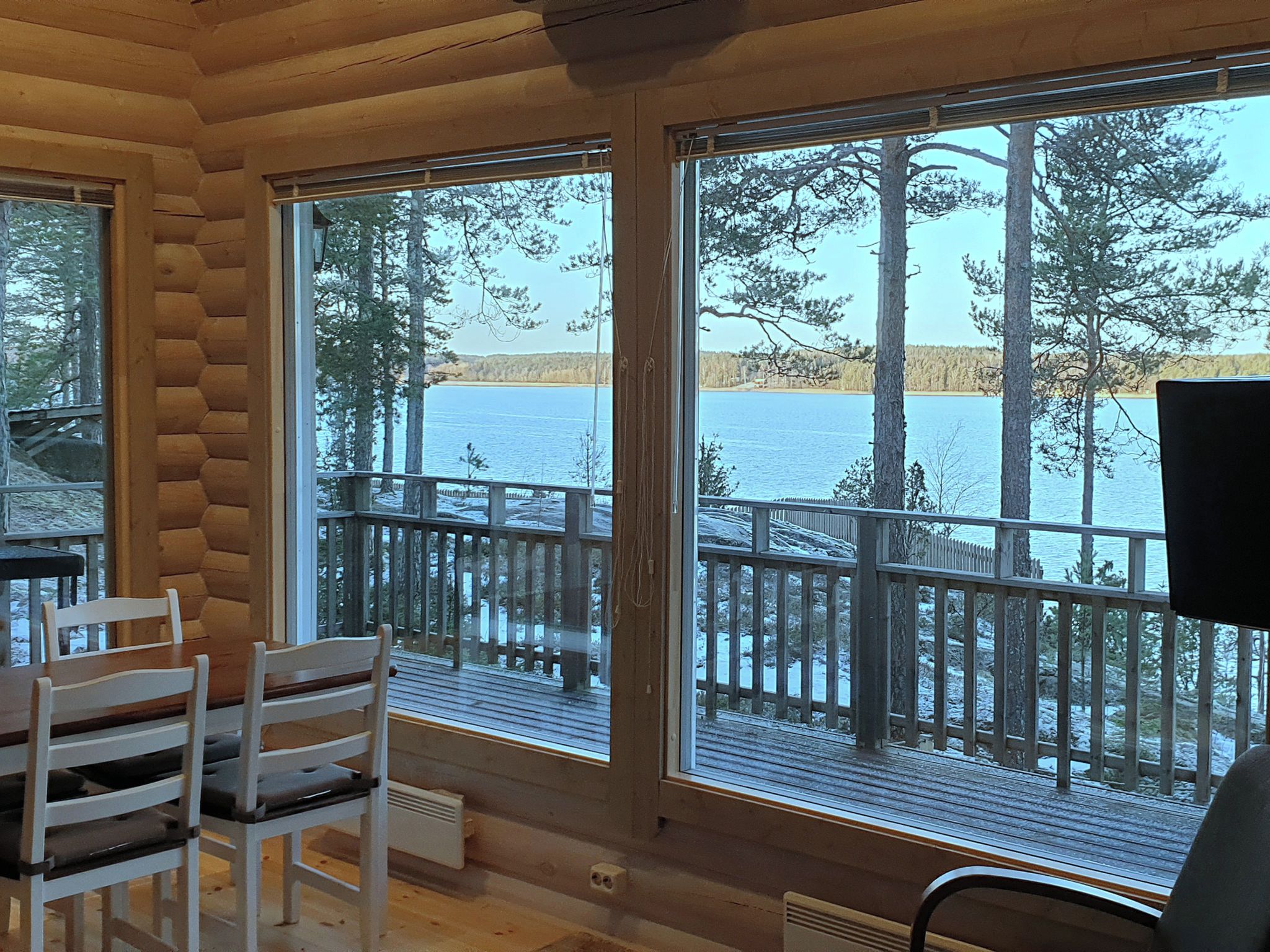 Eine Hütte mit großen Fenstern, die Blick auf einen See und Wald bietet. Im Inneren befinden sich Holzstühle und ein Tisch.