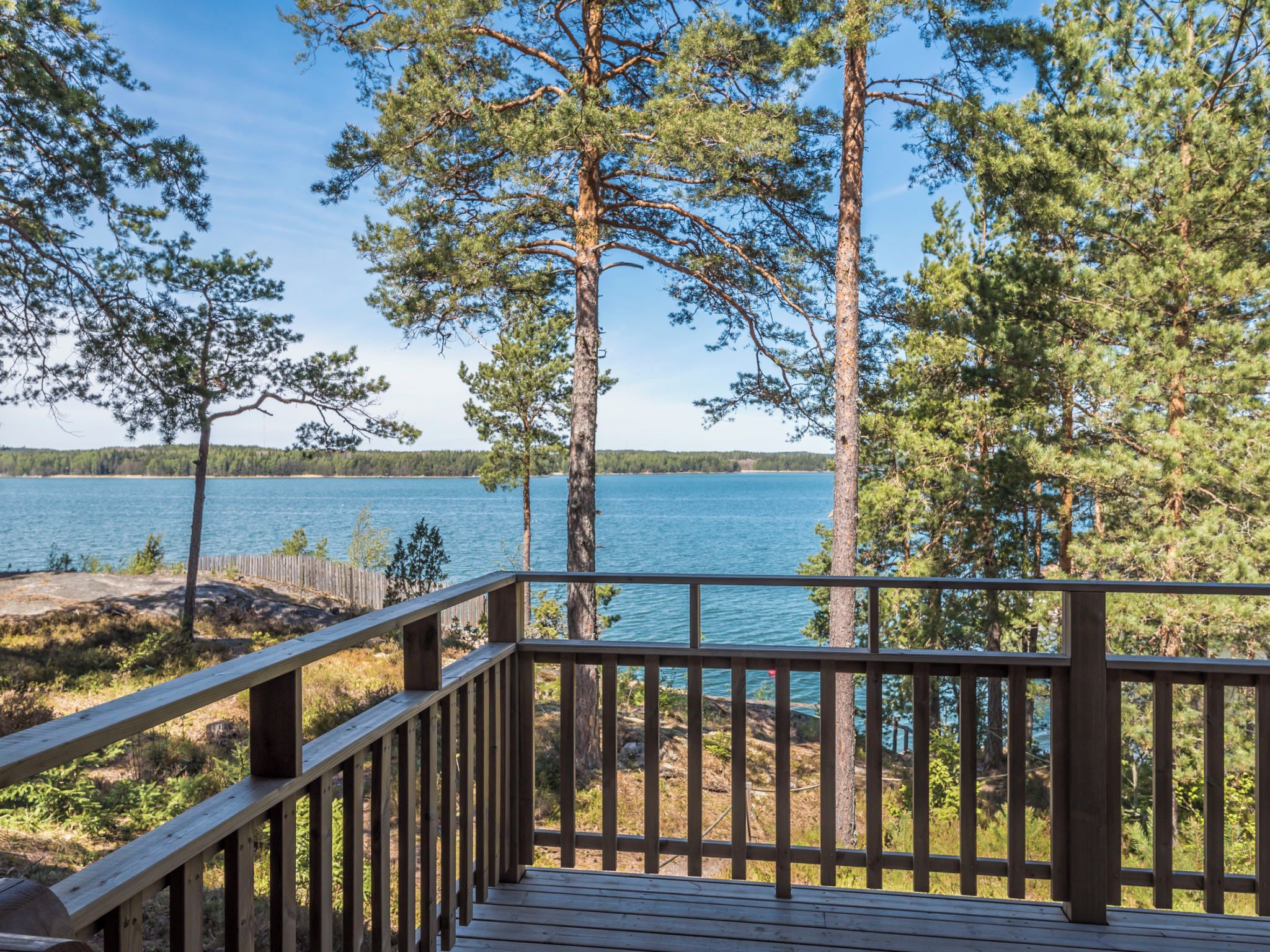 Une terrasse en bois avec une rambarde, donnant sur un lac entouré d’arbres.