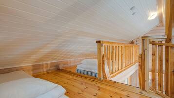A room with a sloped ceiling, wooden flooring, a bed with white bedding, and a wooden railing.