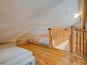 Een kamer met schuine wanden, houten vloeren, een bed met wit beddengoed en een houten leuning.