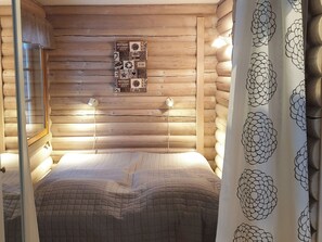 Habitació de cabana de fusta amb un llit, dues làmpades penjades a la paret i un objecte decoratiu a la paret.