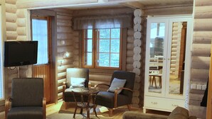 L’intérieur d’une cabane en rondins, avec un téléviseur, deux fauteuils, un canapé et un coin repas.