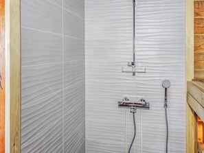 A shower with a vertical hose and a handheld showerhead, a control panel, and a wooden frame on the right.