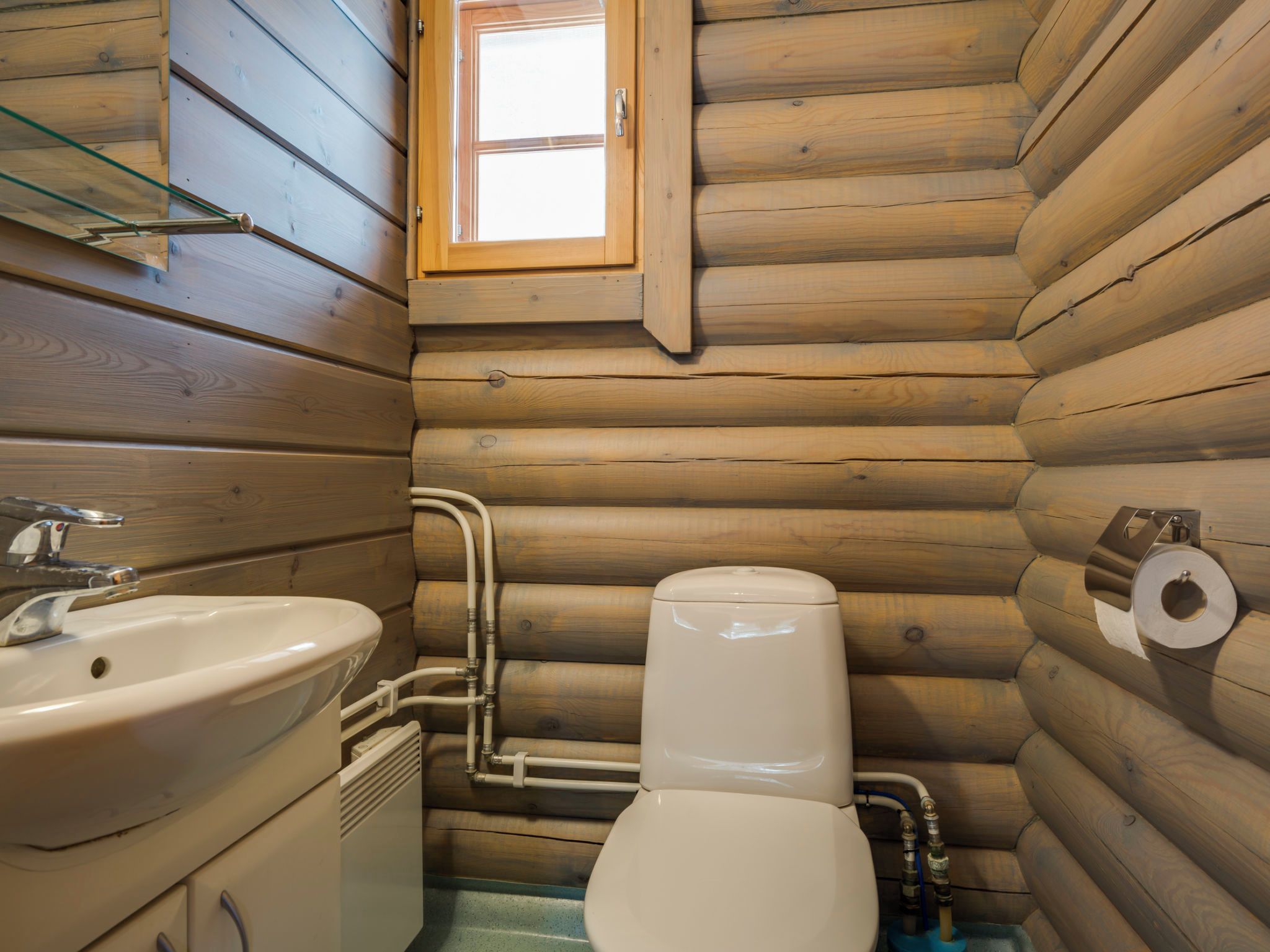 A compact wooden cabin bathroom with a sink, toilet, and a window above the toilet.