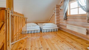 Une chambre aménagée dans un chalet en rondins, avec deux lits, un escalier en bois et une fenêtre avec des rideaux.