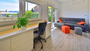 A modern living room with a grey sofa, orange cushions, a black office chair, and a potted plant. - Koalas Nest Home & Apartments by Interhome (Opatija/Matulji)