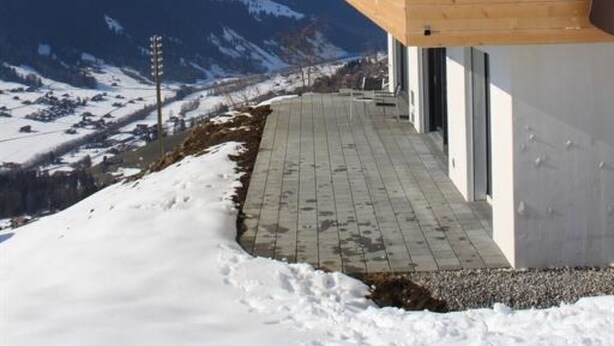 A modern wooden building with a balcony overlooking a snowy mountain landscape.