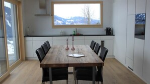 A modern kitchen with a wooden dining table, black chairs, and a large window overlooking a snowy landscape.