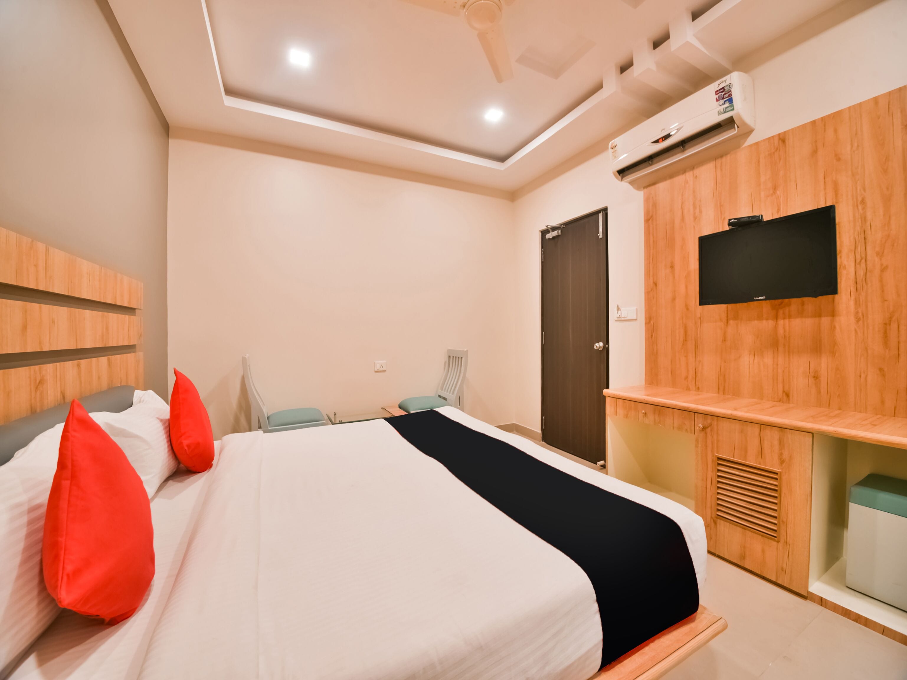 A modern hotel room with a large bed, a TV mounted on the wall, and a wooden cabinet.