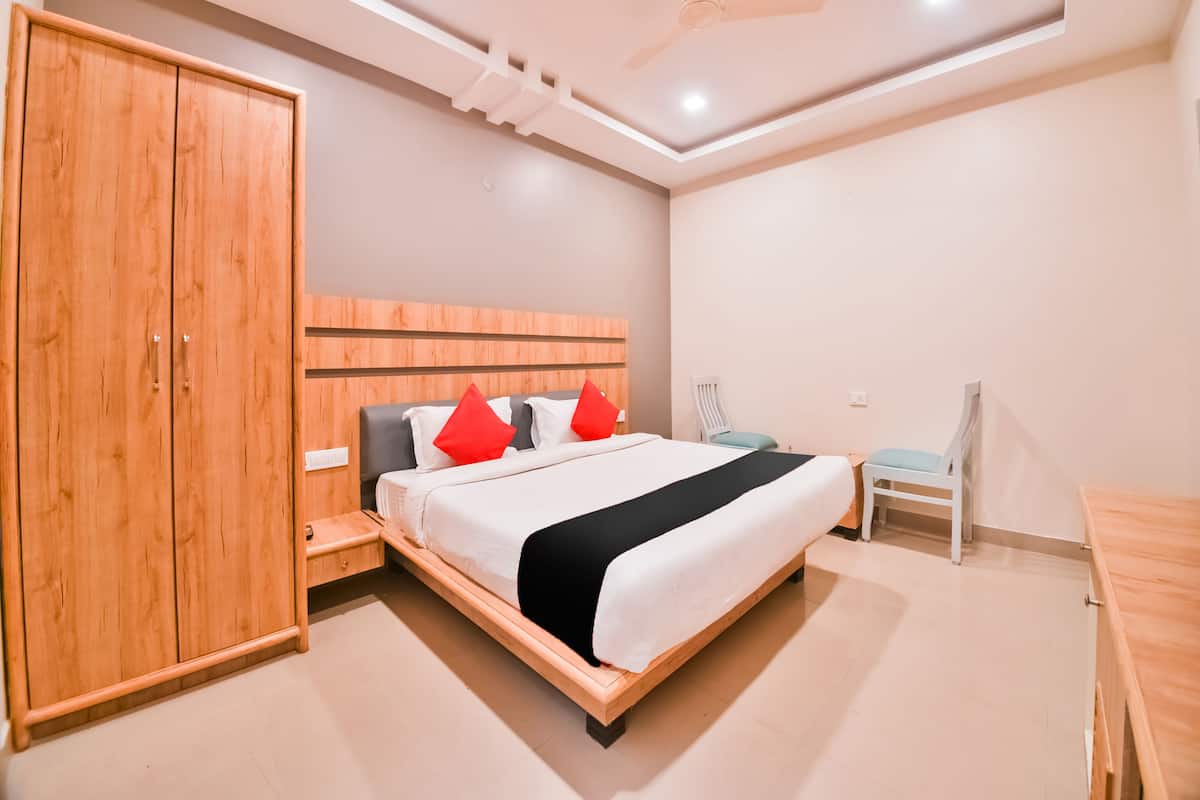 A modern bedroom with a wooden wardrobe, a bed with white bedding and red pillows, a ceiling fan, and a small table.