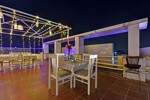 An outdoor dining area with white chairs and tables, string lights, and a view of the cityscape. - Ardency Inn by Park Tree Udaipur (Udaipur)