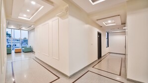 A modern hallway with a polished floor, recessed ceiling lights, and a seating area with green sofas. - Ardency Inn by Park Tree Udaipur (Udaipur)