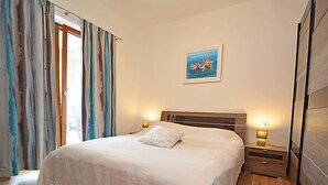 Un dormitorio con una cama grande, cabecera de madera, dos mesitas de noche con lámparas, un cuadro en la pared y vistas a través de una puerta corredera.