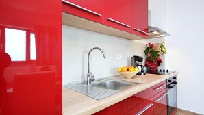 Una cocina moderna con armarios rojos, un lavamanos de acero inoxidable y una encimera con un frutero.