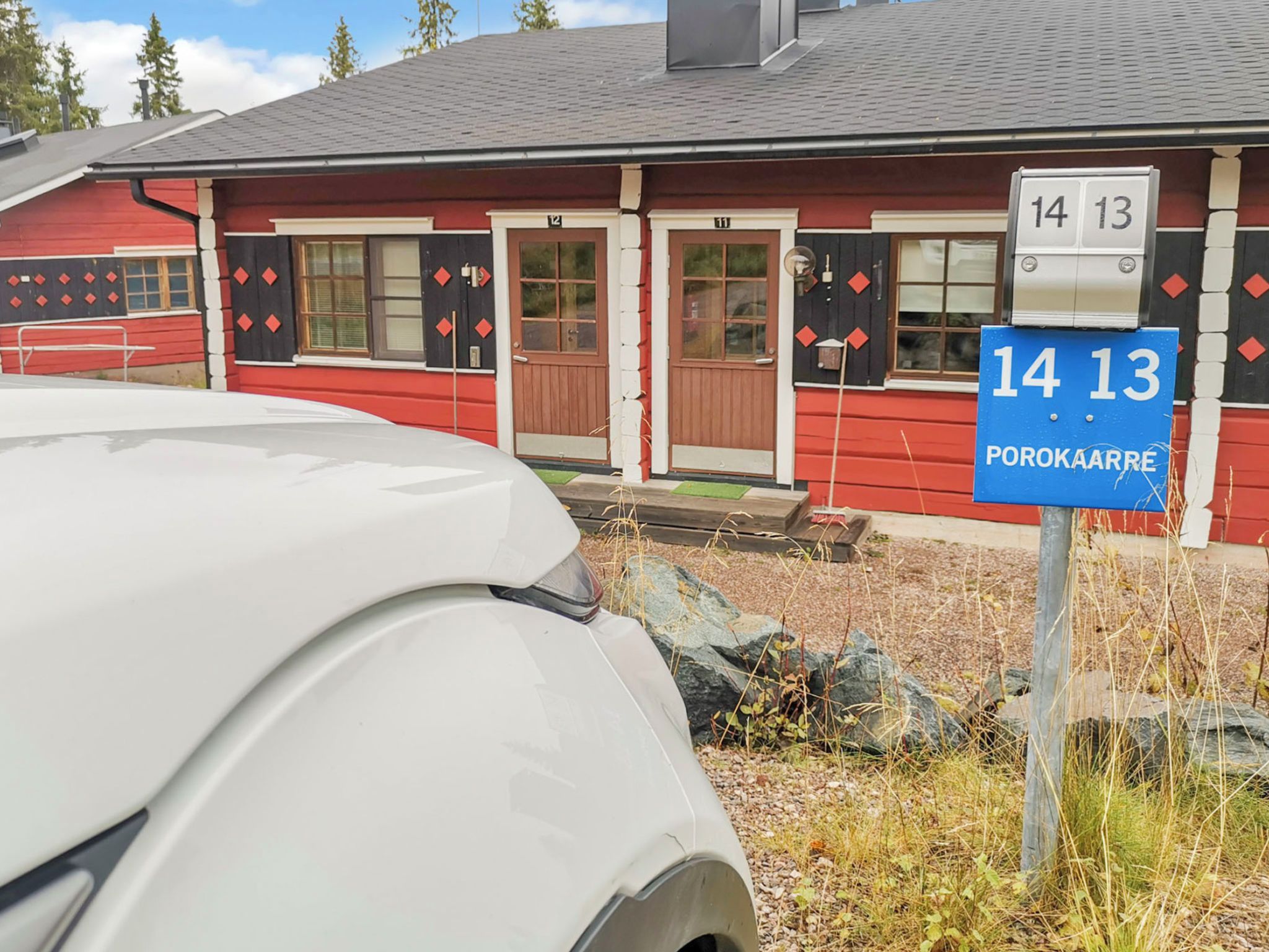 Un edificio rojo con puertas numeradas, un coche blanco estacionado al frente y un letrero azul con el número 14 13.