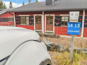 Un edificio rojo con puertas numeradas, un coche blanco estacionado al frente y un letrero azul con el número 14 13.