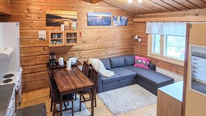 Interior de una cabaña de madera con comedor, sofá y cocina.