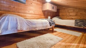 Una cabaña con dos camas, paredes de madera, una lámpara en el techo y un cuadro enmarcado.