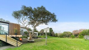Una casa moderna con una escalera de madera que conduce a una terraza, rodeada por un césped cuidado y árboles.