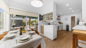 Una cocina moderna con armarios blancos, un comedor con una mesa dispuesta para cuatro personas y un amplio ventanal con vistas a un jardín.