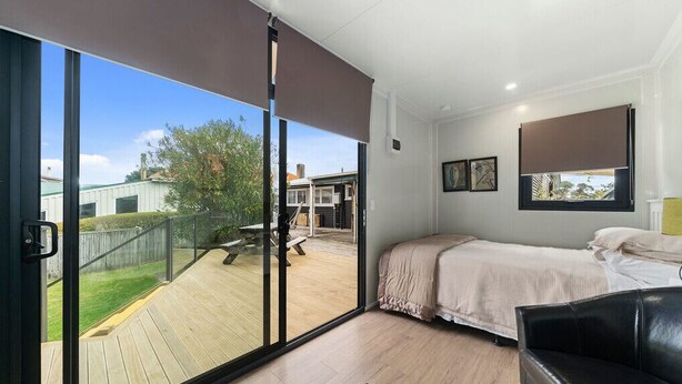 Un dormitorio con un amplio ventanal corredero que da a una terraza, una cama, un sillón de cuero negro y una ventana con persiana.