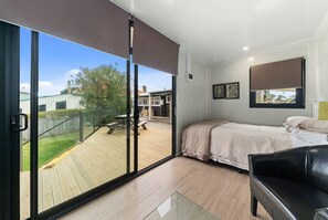 Une chambre avec une grande porte-fenêtre coulissante donnant sur une terrasse, un lit, un fauteuil en cuir noir et une fenêtre avec un store.