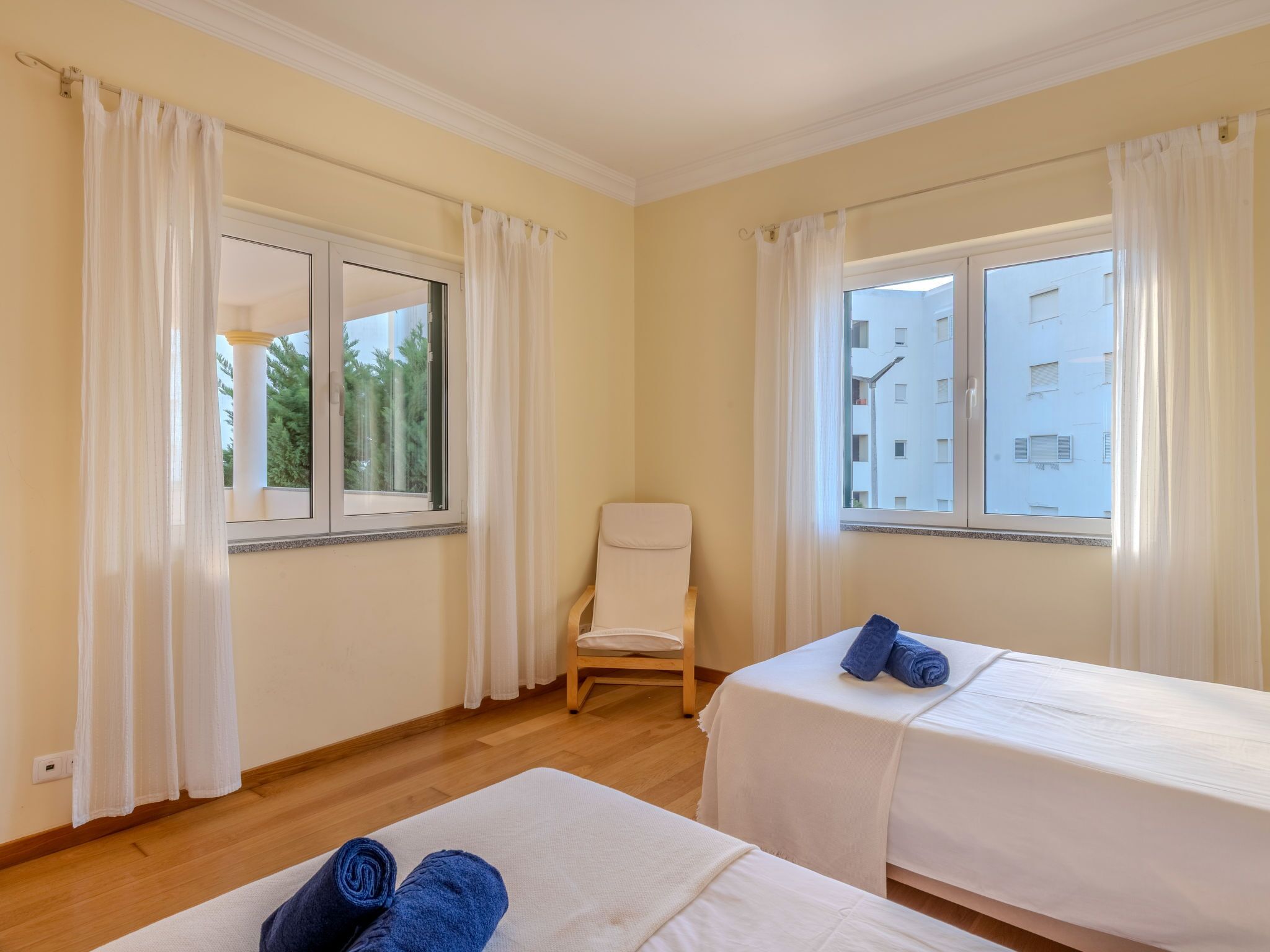 Une chambre d’hôtel avec deux lits, une chaise et de grandes fenêtres avec des rideaux.