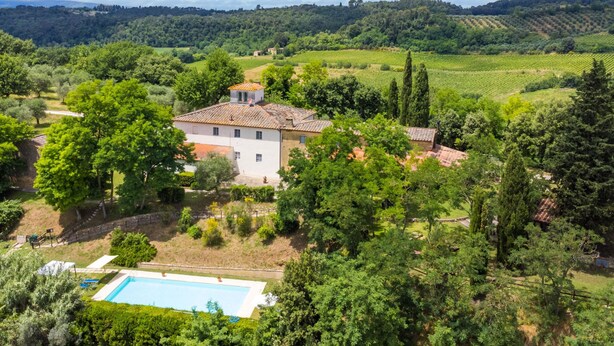 Uma villa com piscina, rodeada por vegetação exuberante e vinhedos ao fundo.