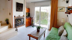 Ett vardagsrum med en öppen spis, en soffa, ett soffbord och utsikt över trädgården genom en skjutdörr i glas.