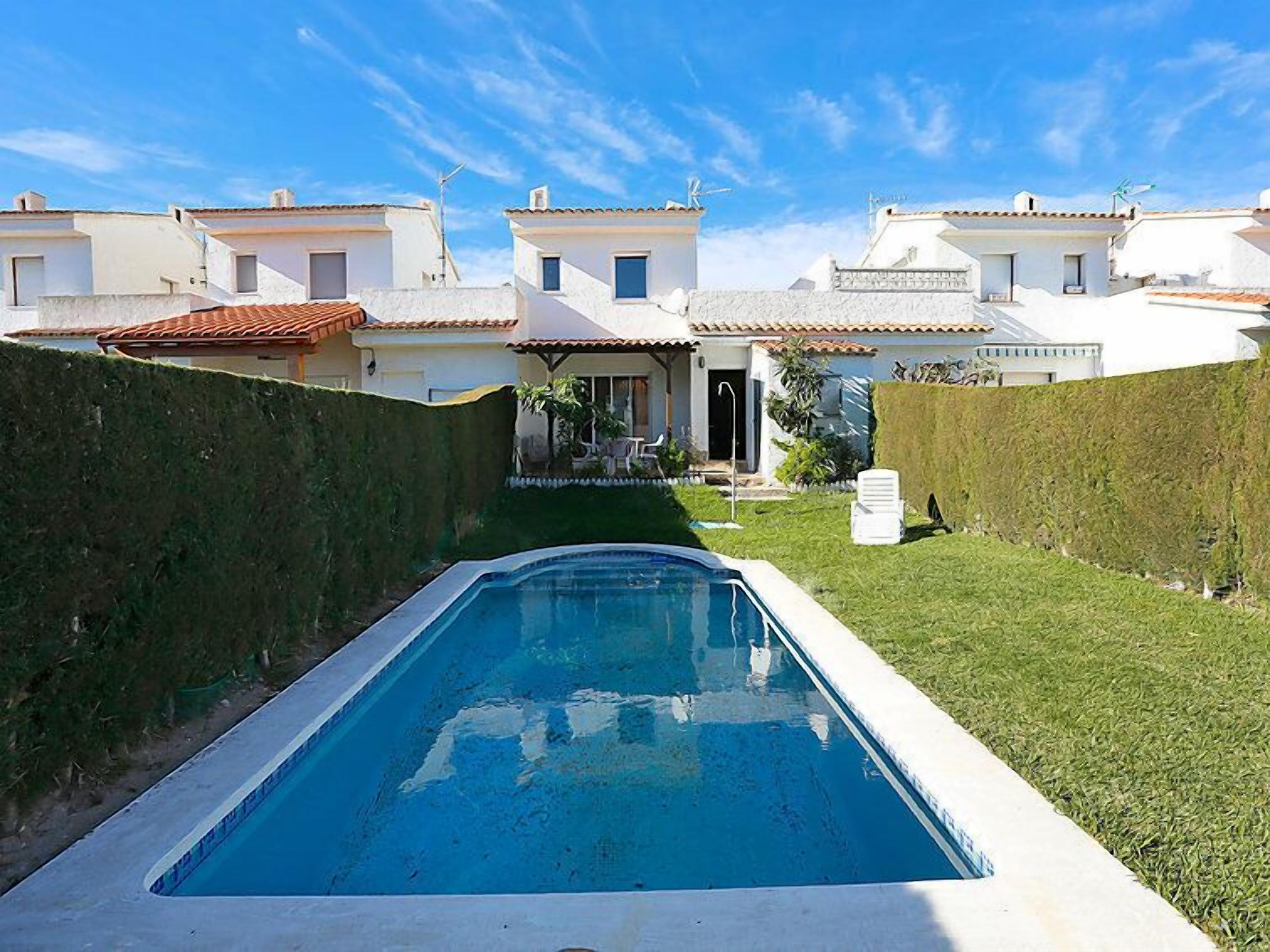 A swimming pool with a clear blue water surface, surrounded by a well-maintained lawn and a hedge.