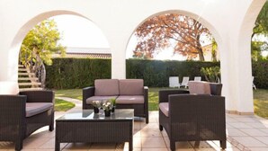 Un espacio al aire libre con mobiliario de mimbre, incluyendo un sofá y sillas, y una mesa de centro de vidrio.