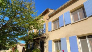 A two-story building with blue shutters, a patio with outdoor seating, and potted plants. - de la Roque by Interhome (Carpentras)