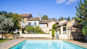 A swimming pool with a clear blue water surface, surrounded by a paved walkway. In the background, there is a two-story building with a tiled roof and a small attached structure with a glass door. - de la Roque by Interhome (Carpentras)