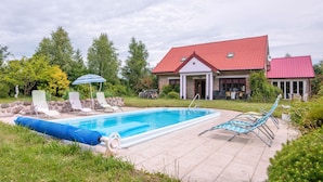 Une piscine avec des chaises longues, un parasol et une maison avec un toit rouge.