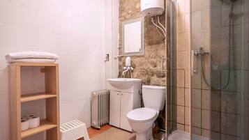 Een badkamer met toilet, wastafel en douche. Er is een houten plank met handdoeken en een opstapje.