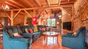 Un salon chaleureux avec une cheminée, des poutres en bois et une tête de tigre empaillée accrochée au mur.